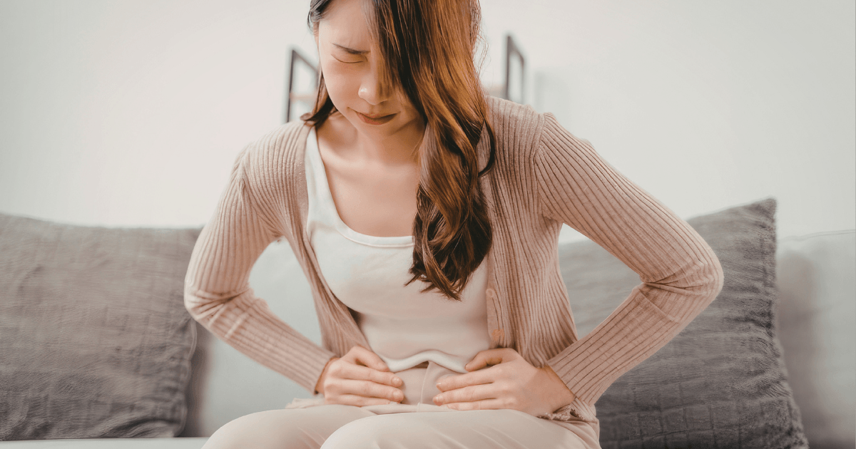 お腹を押さえてつらそうに座る女性。春の胃腸不調や胃の重さをイメージした写真。