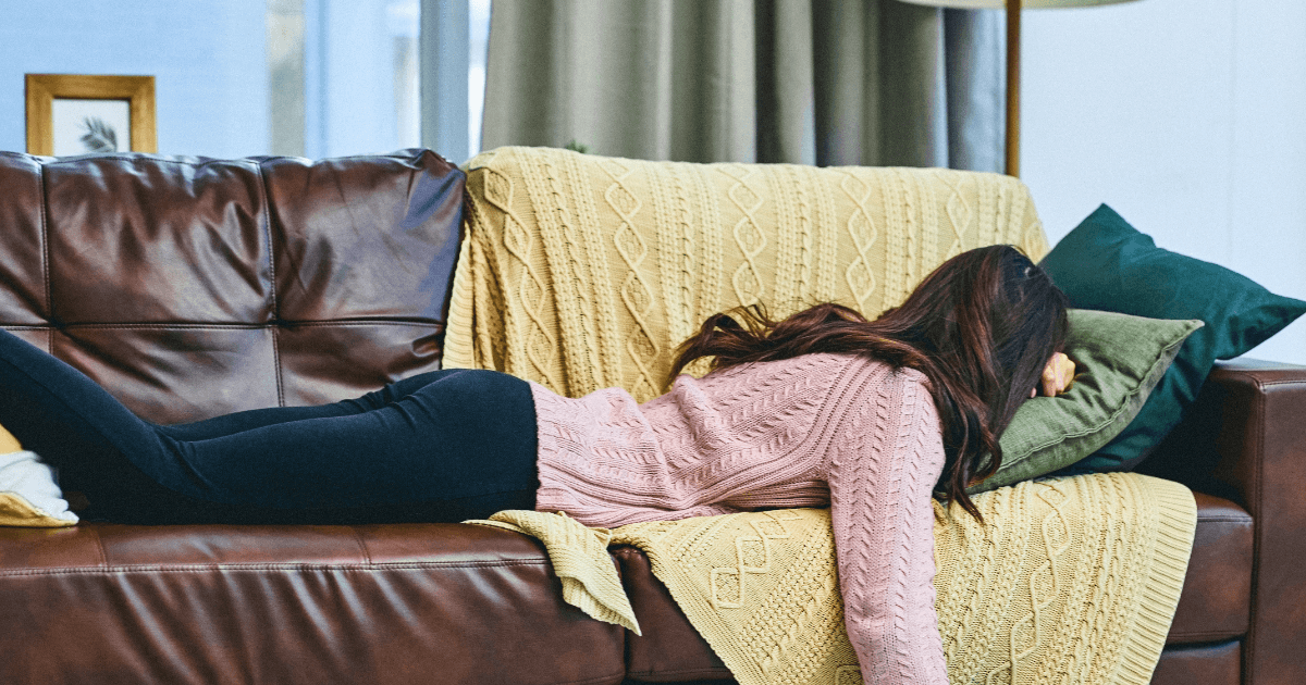ソファにうつ伏せで寝転び、だるそうに動けずにいる女性。春の疲れややる気の出なさをイメージした写真。